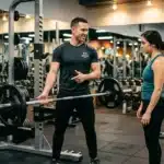 Homme entraîneur aide femme avec haltère en salle sport.